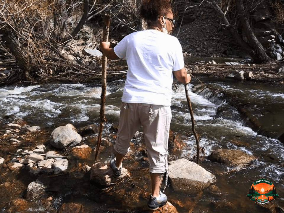 Woman crossing a rocky stream with two walking sticks during a nature hike